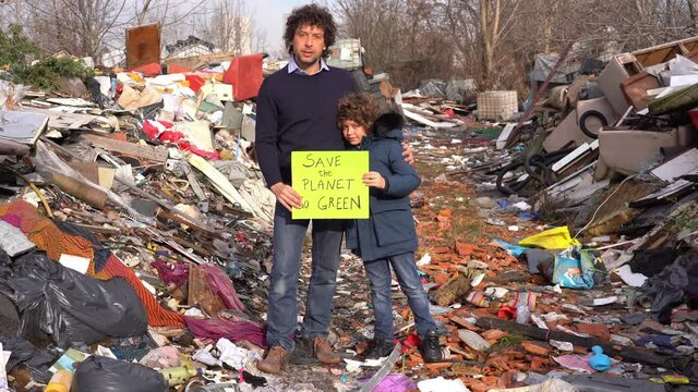 Father 40 years old and son child 7 ecologist holding a sign with the words save the planet go green, protest against climate change, global warming and atmospheric pollution in a garbage dump waste