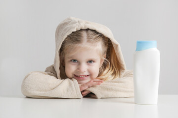 Portrait of happy little girl wearing terry bathrobe with blank plastic cosmetic bottle