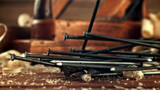 A bunch of nails fall on the table. On a wooden background. Filmed is slow motion 1000 frames per second.