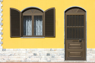 Brown window with lace curtain and door on a yellow facade