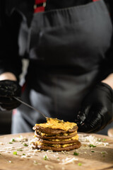 the chef prepares liver pie in the kitchen. Close-up of female hands in gloves apply filling between liver pancakes. c