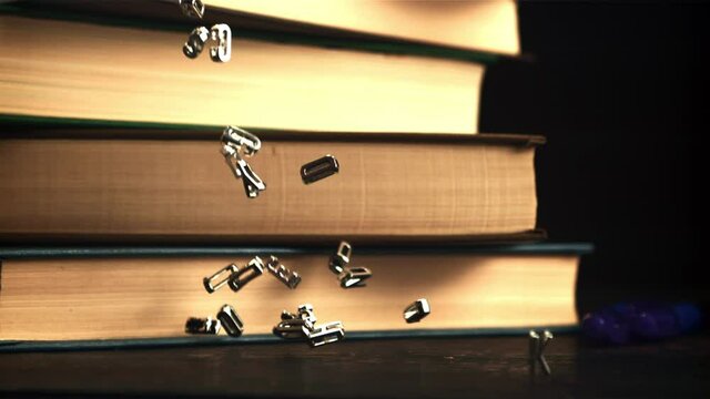 The metal letters of the English alphabet fall on the table. On a black background. Filmed is slow motion 1000 frames per second.