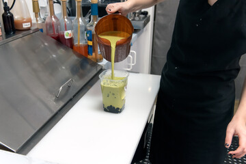 Hands pouring smoothie boba ingredients from a pitcher into the cup for a gradient mix of flavors...