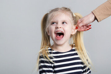 Disobedient little girl being punished by ear pulling, studio shot