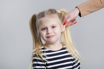 Disobedient little girl being punished by ear pulling, studio shot