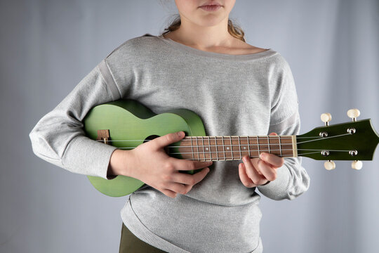 
girl learning to play the ukulele. green ukulele in the hands of a girl