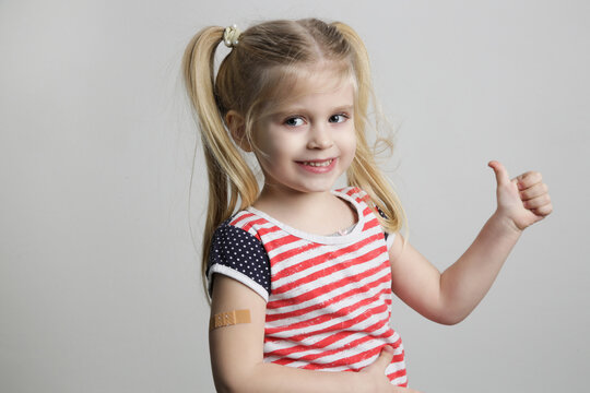 Child vaccination. Little girl showing thumb up gesure and adhezive arm bandage, studio shot.