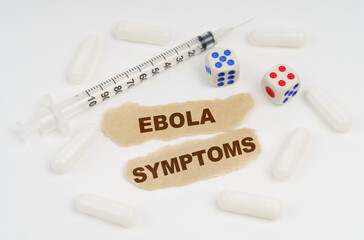 On a white surface lies a syringe, pills, dice and pieces of paper with the inscription - EBOLA SYMPTOMS