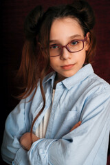 portrait of a young teenage girl up to the waist in a blue shirt with glasses and with long hair in a hairstyle