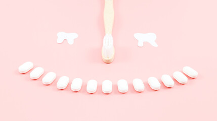Bamboo toothbrush, chewing gums in the forem of a smile and paper eyes teeth on a soft pink