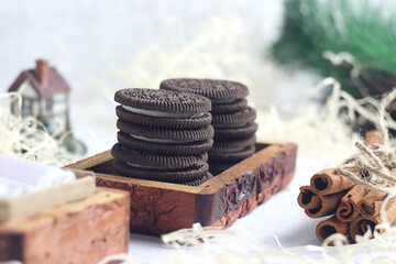 Cookies with a milk nightstand in a wooden box on the table. There are cinnamon sticks nearby. There is a branch of a Christmas tree behind.