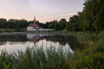 Prioratsky aka Priory palace in Gatchina stands on the shore of the pond. It is surrounded by a green forest. Small mansion, resembling a medieval 18th century European monastery with red tall spires.