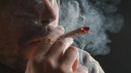 Man smoking a marijuana weed joint, inhaling cannabis smoke. - obrazy, fototapety, plakaty