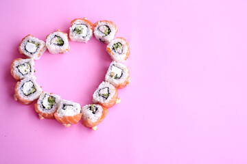Sushi set in the shape of a heart on pink background. Valentine day or March 8th food concept.The concept of a romantic dinner at a sushi bar for February 14th.  
