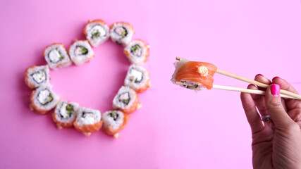 Sushi set in the shape of a heart on pink  background. Valentine day or March 8th food concept.The concept of a romantic dinner at a sushi bar for February 14th.	