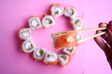 Sushi set in the shape of a heart on pink  background. Valentine day or March 8th food concept.The concept of a romantic dinner at a sushi bar for February 14th.	