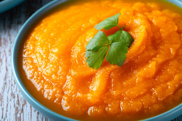A bowl of pumpkin soup on a blue wooden table.