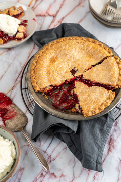 Sliced cherry pie in pie tin on cooling rack with ice cream