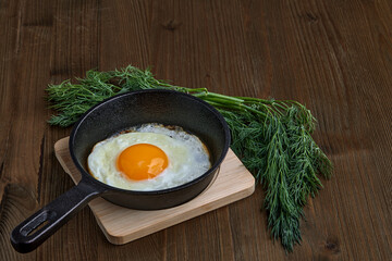 Fried chicken egg in a small frying pan with a stand, a bunch of dill