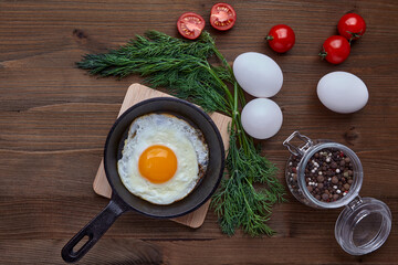 Fried egg in a small skillet with a stand, a bunch of dill, tomatoes