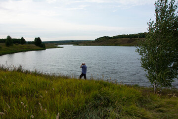 Lake shore with trees and tall grass, a photographer in the Russian expanses, August evening in Russia.