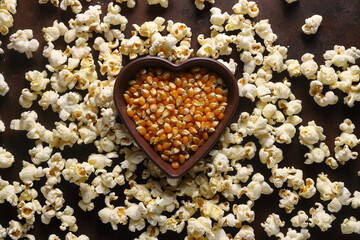 Popcorn in a brown wooden plate in the shape of a heart on a wooden table. Popcorn is laid out on the table.