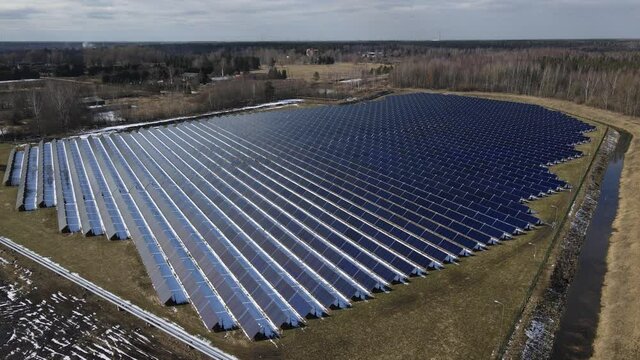 Solar panels grid in solar farm. Spring day after winter snow. Solar power green energy. Renewable energy to stop climate change. Sustainable electricity sources. Aerial fly over drone shot.