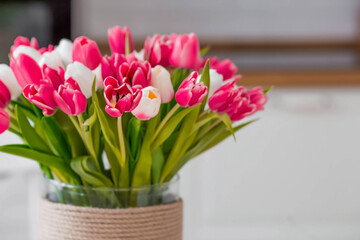 Fototapeta na wymiar A bouquet of tulips on a white table. In the background, the interior of a white kitchen in the Scandinavian style. The concept of home comfort.The concept of International Women's Day on March 8.