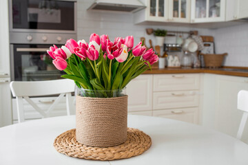 A bouquet of tulips on a white table. In the background, the interior of a white kitchen in the Scandinavian style. The concept of home comfort.The concept of International Women's Day on March 8.