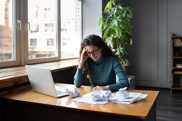 Stressed tired businesswoman exhausted overwhelmed at desk with laptop and crumpled paper....