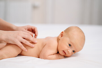the baby lies on his tummy on a white sheet. and mom's hands massage the back. 