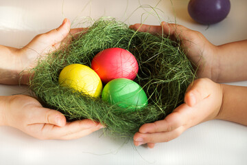 childrens hands hold nest with painted eggs, easter tradition concept