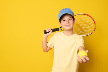 Smiling boy playing tennis holding racket isolated on yellow background