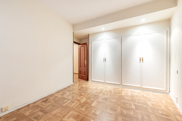 Empty bedroom with four body white wood fitted wardrobes with chestnut hardwood flooring