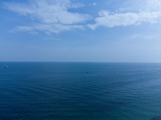 Blue horizon, where the cloudy sky and the blue sea converge. Ships and boats are barely visible on the water.