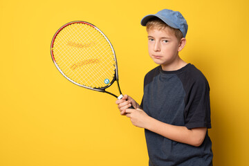 Smiling boy playing tennis holding racket isolated on yellow background