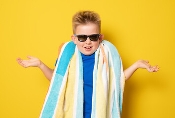 Cute doubtful boy wearing sunglasses in summer outfit standing over yellow background.