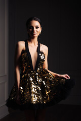 Graceful, tanned, elegant young woman in black evening dress posing in vintage interior. Fashion...