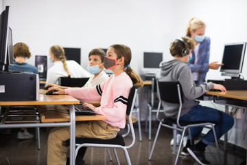 Fototapeta premium Group of young girls and boys in face masks sitting in computer classroom and exercising.