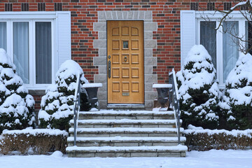 Traditional brick house with wood grain front door and snow covered shrubbery