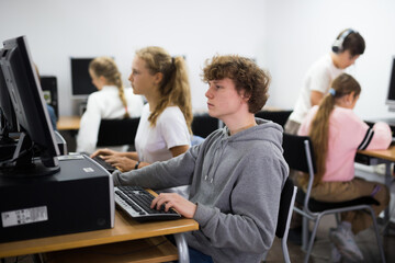 Portrait of a fifteen-year-old schoolboy sitting at a computer in the class at a informatics lesson