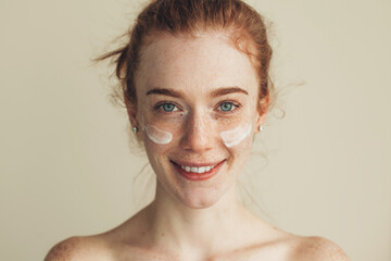 Portrait of a caucasian red haired woman with freckles having on cheeks anti aging cream and smile...
