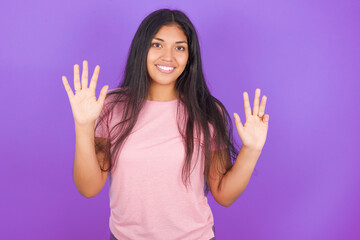 Hispanic brunette girl wearing pink t-shirt over purple background showing and pointing up with fingers number nine while smiling confident and happy.