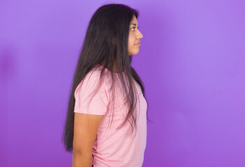 Hispanic brunette girl wearing pink t-shirt over purple background looking to side, relax profile pose with natural face with confident smile.