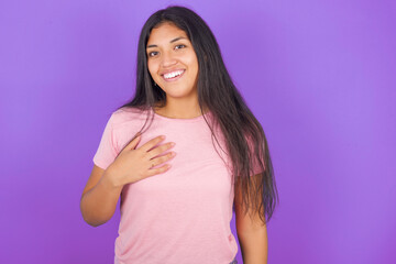 Hispanic brunette girl wearing pink t-shirt over purple background smiles toothily cannot believe eyes expresses good emotions and surprisement