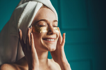 Caucasian woman in towel, puts on golden hydrogel patches and smiling. Under eye collagen gold...