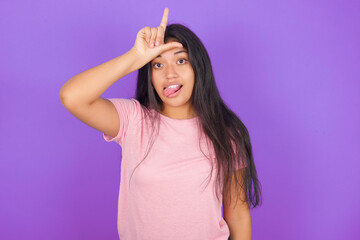 Hispanic brunette girl wearing pink t-shirt over purple background gestures with finger on forehead...