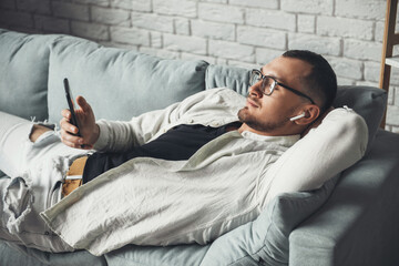 Caucasian man relaxing on sofa after working, listening to music in airpods. Mobile communication....
