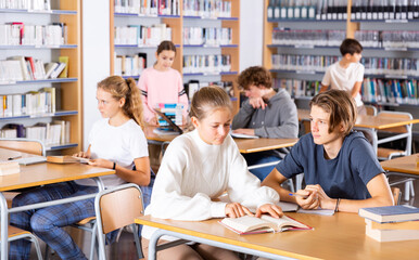 Obraz premium Schoolchildren studying in the school library write down a summary from a textbook in a exercise book, discussing topical ..issues