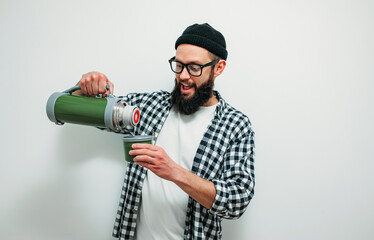 Young man with a beard holds a thermos and drinks hot tea isolated on white background